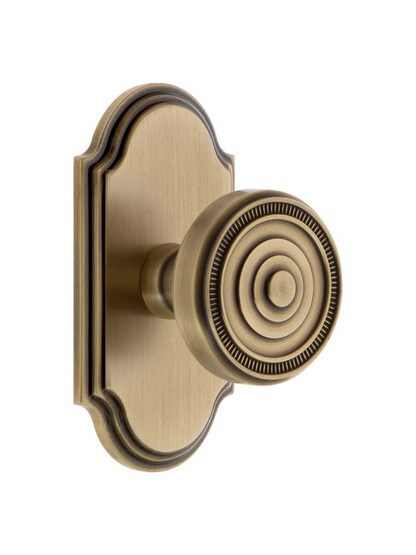 Grandeur Arc Rosette Door Set with Soleil Knobs in Antique Brass.